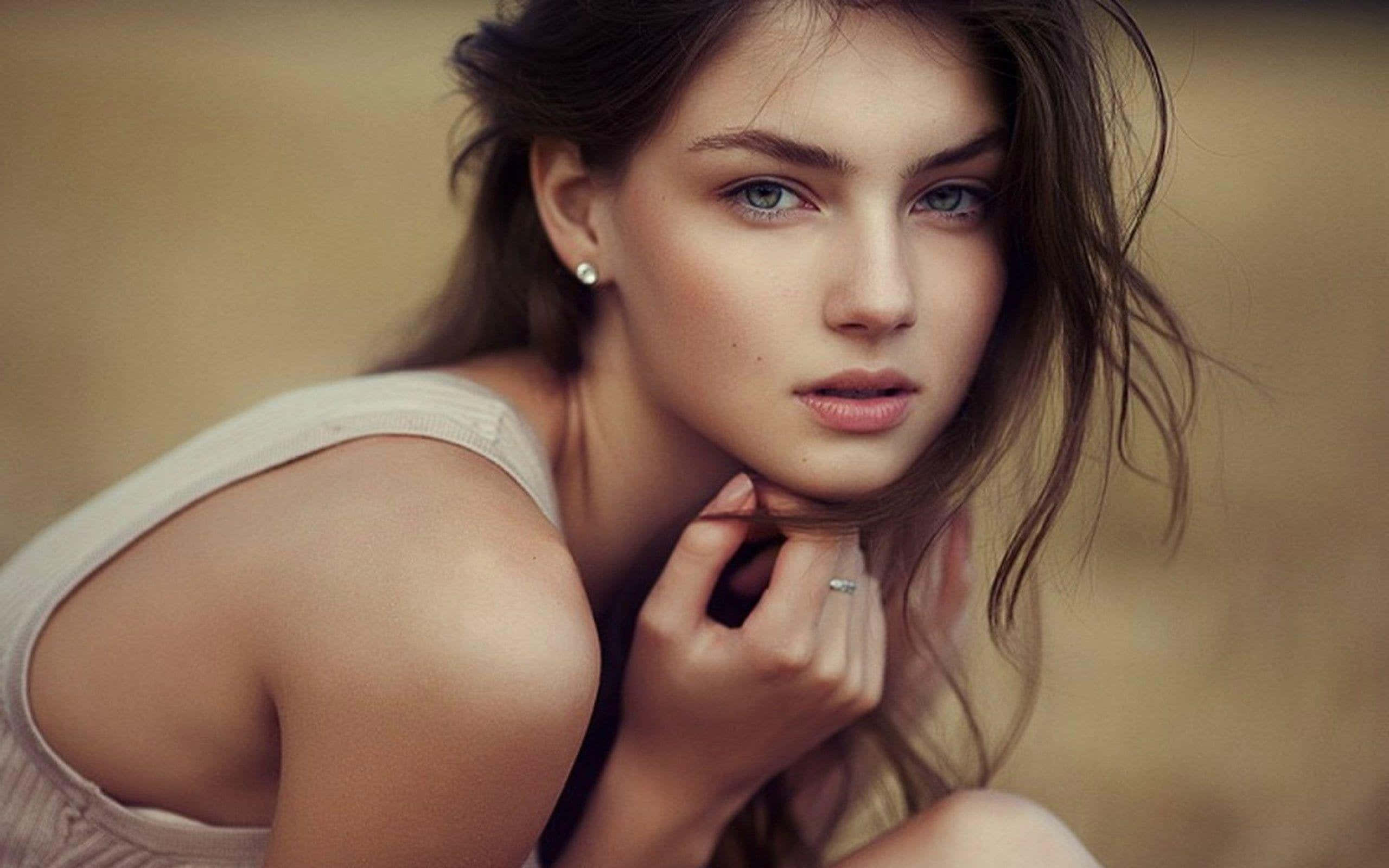 Captivating Ukrainian Beauty 壁紙 — 一位年輕女性，擁有引人注目的藍色眼睛和凌亂的棕色頭髮，輕輕地將下巴靠在手上凝視著。