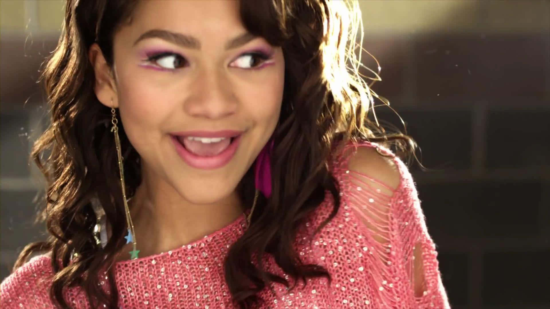 Zendaya 桌布 壁紙 — 一位年輕女性，擁有捲曲的棕色頭髮，身穿粉紅色閃亮上衣，在溫暖的陽光下側視，露出俏皮的笑容。