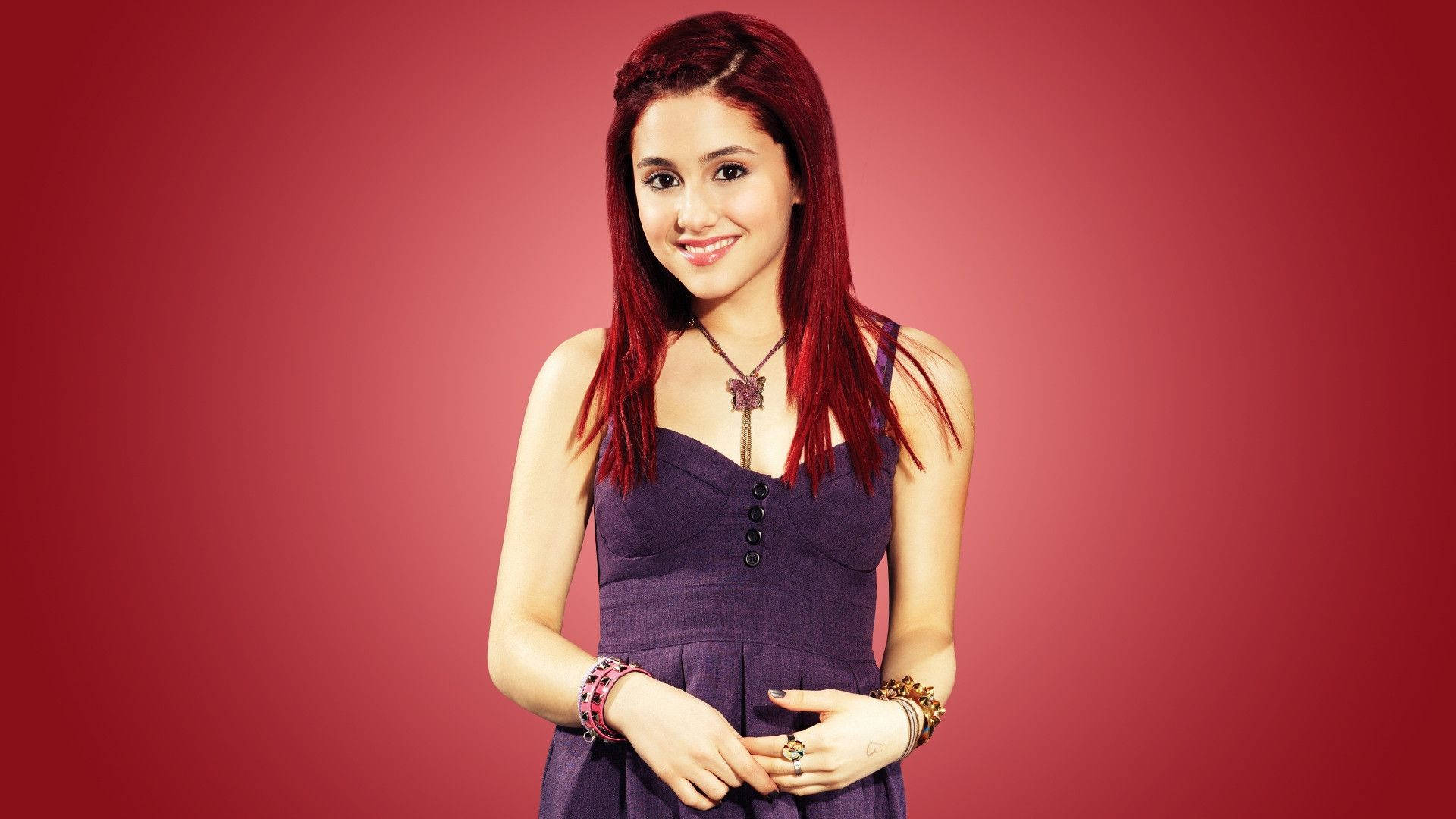 Ariana Grande Dazzles in Red Hair 壁紙 — 一位年輕女性，擁有鮮豔的紅髮，穿著紫色連衣裙，在純紅色背景前溫暖地微笑。