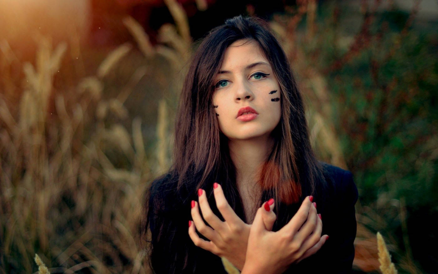 Beautiful Woman 桌布 壁紙 — 一位年輕女性，臉上畫著貓咪妝容，塗著紅色指甲，站在金色的草叢中，若有所思地凝視著鏡頭。