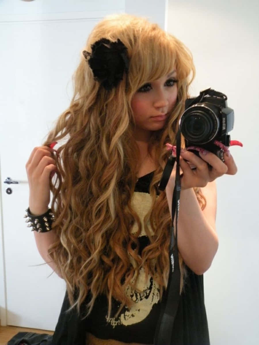 Gyaru 桌布 壁紙 — 一位年輕女性，長著波浪形金色長髮，戴著黑色花朵髮夾，在一個樸素的房間裡用單反相機對著鏡子自拍。