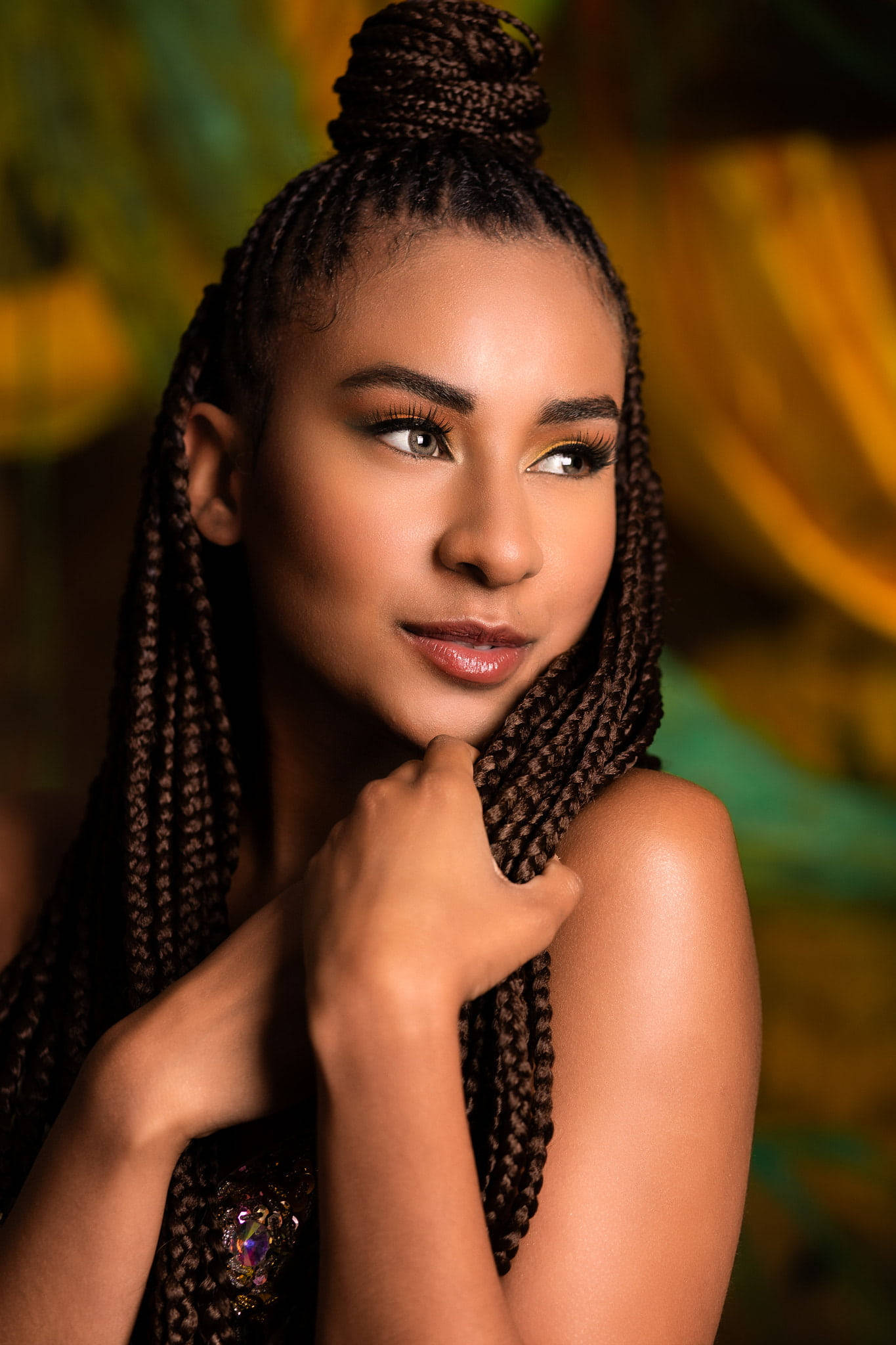 Beautiful Woman 桌布 壁紙 — 一位年輕女性，長辮子盤成高髻，在溫暖模糊的背景中輕柔地凝視，同時觸摸她的辮子。