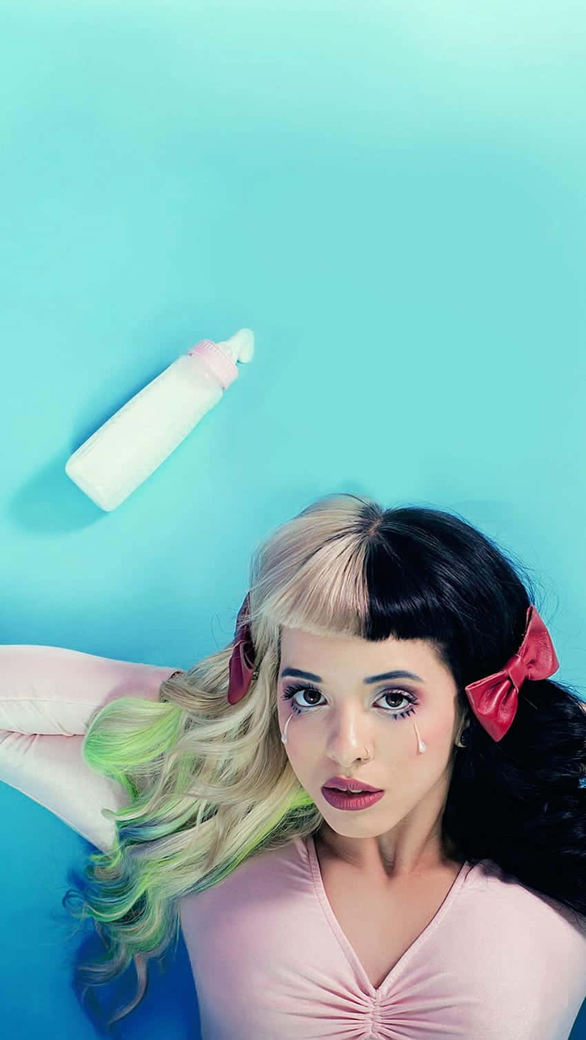 Melanie Martinez 桌布 壁紙 — 一位年輕女性，頭髮半黑半金，戴著紅色蝴蝶結，躺在藍綠色背景上，附近有一個白色瓶子，淚水從她的臉上流下。
