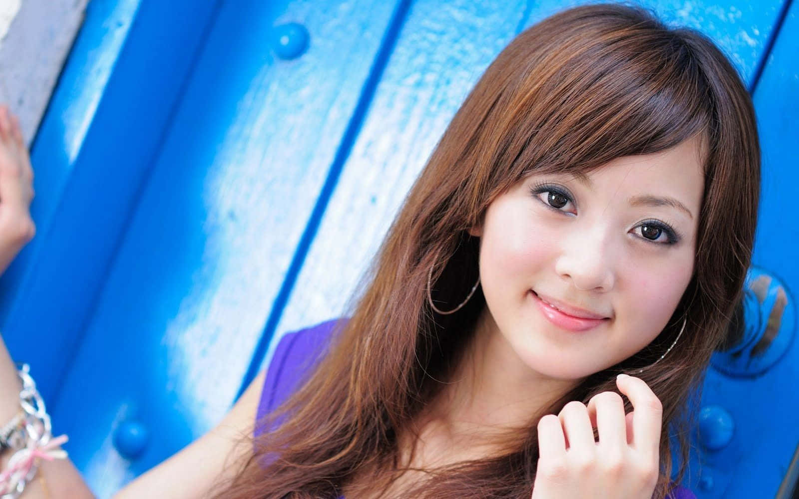 Beautiful Girls 桌布 壁紙 — 一位年輕女性留著長長的棕色頭髮，在鮮豔的藍色木質背景下溫柔微笑。