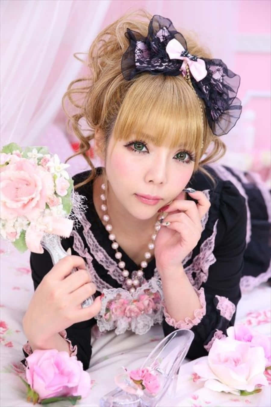 Gyaru 桌布 壁紙 — 一位年輕女性身穿黑色蕾絲洛麗塔連衣裙，手捧粉紅玫瑰束，下巴擱在手上。