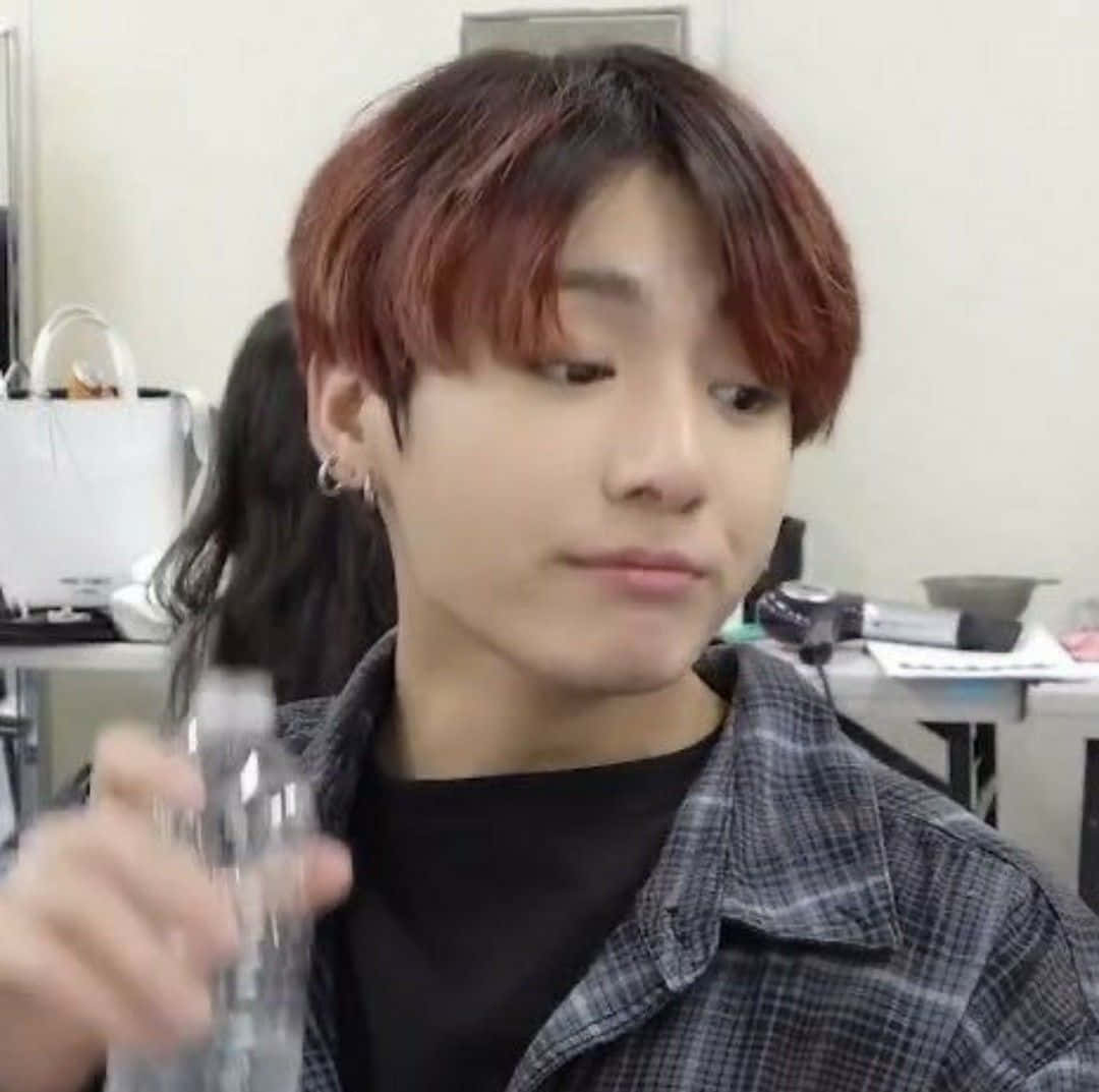 Bts Meme 桌布 壁紙 — 一位年輕男子，帶有紅褐色頭髮和耳環，在後台房間裡拿著一個水瓶。
