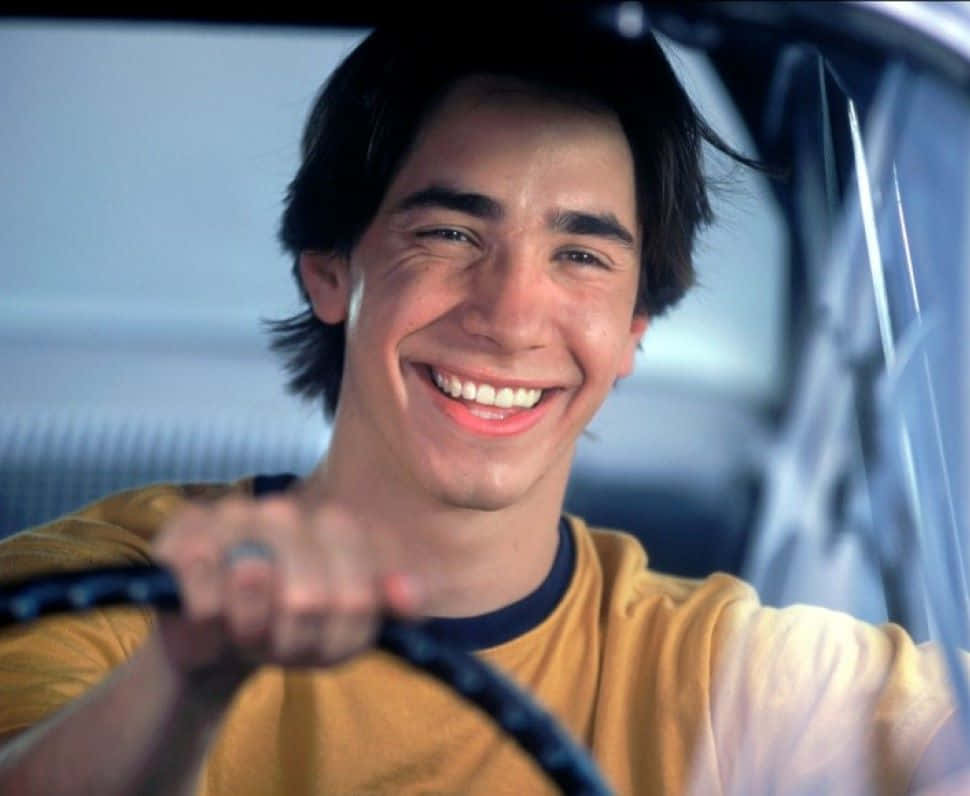 Justin Long 桌布 壁紙 — 一位年輕男子在車內緊握方向盤，滿臉喜悅。