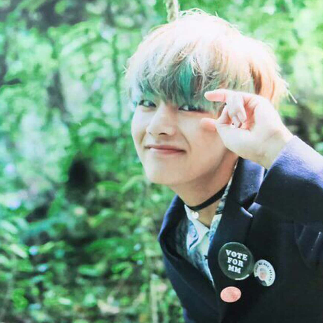 Taehyung Cute 桌布 壁紙 — 一位年輕男子擁有色彩繽紛的頭髮，在茂密的綠色森林中微笑，手靠近臉龐。
