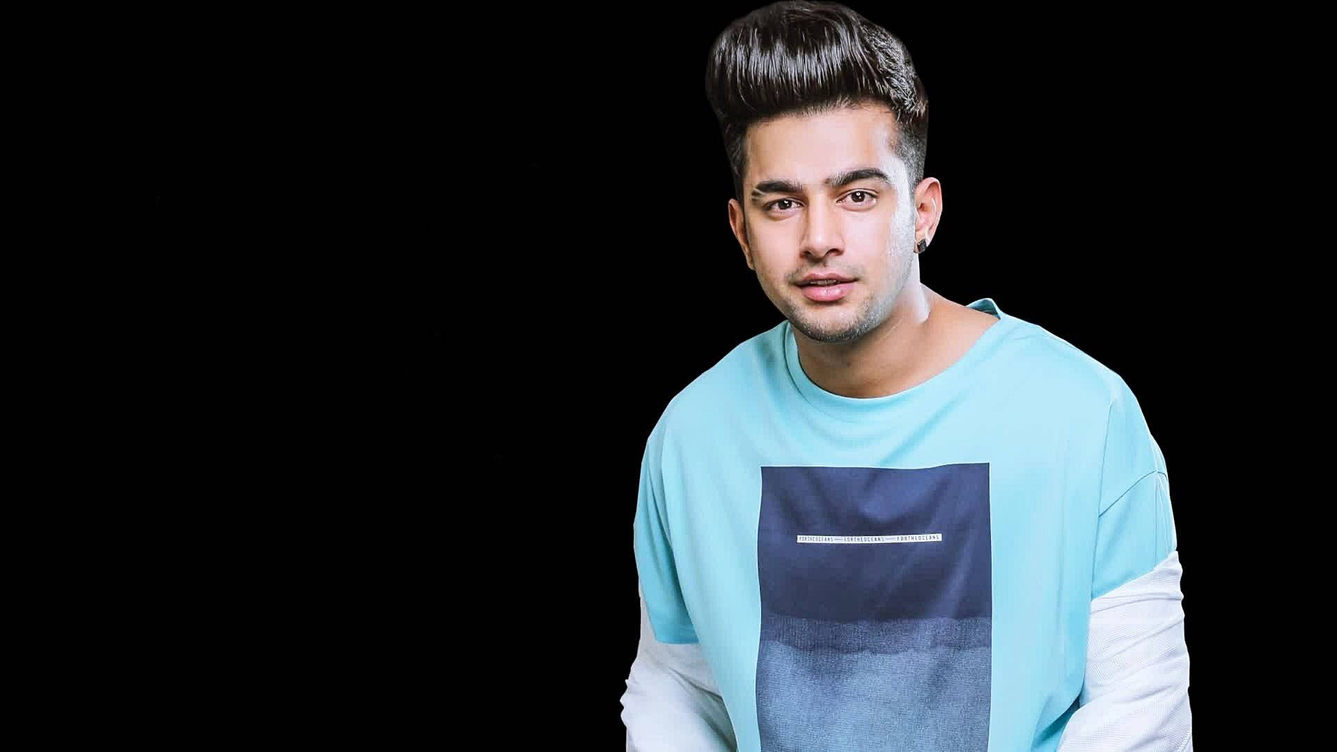 Indian 桌布 壁紙 — 一位年輕男子梳著時尚髮型，穿著淺藍色和白色分層襯衫，背景為純黑色。