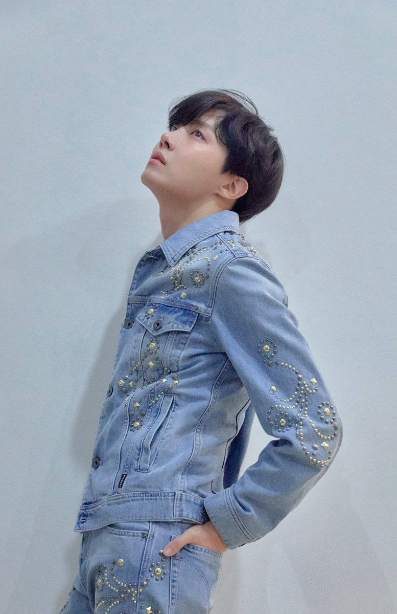 J-hope Denim On Denim 壁紙 — 一位年輕男子身穿淺藍色牛仔外套和褲子，飾有金色鉚釘，抬頭望著純灰色的牆壁。