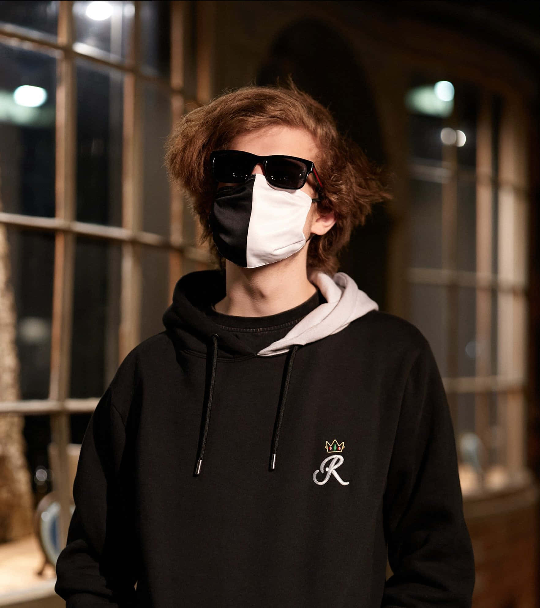 ranboo 桌布 壁紙 — 一位年輕的捲髮人士戴著黑白口罩和太陽眼鏡，夜晚在室內靠近窗戶站立。