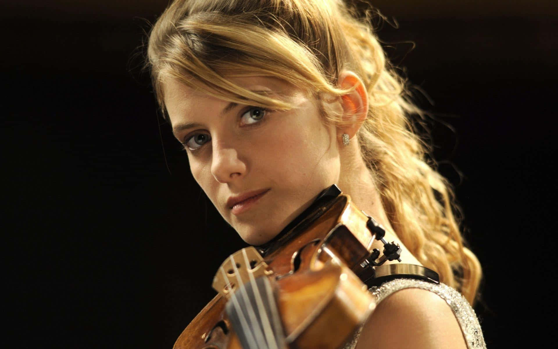 Mélanie Laurent 桌布 壁紙 — 一位年輕的金髮小提琴手在黑暗背景下專注地凝視著，手中握著她的樂器。