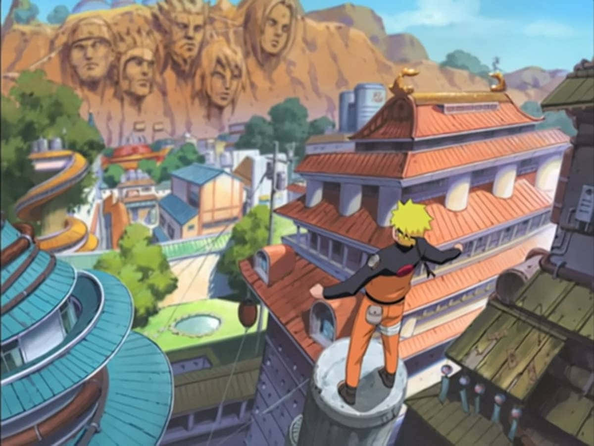 Naruto Village 桌布 壁紙 — 一位年輕的金髮忍者站在塔頂，俯瞰著一個充滿活力的動畫村莊，遠處的懸崖上有巨大的雕刻面孔。
