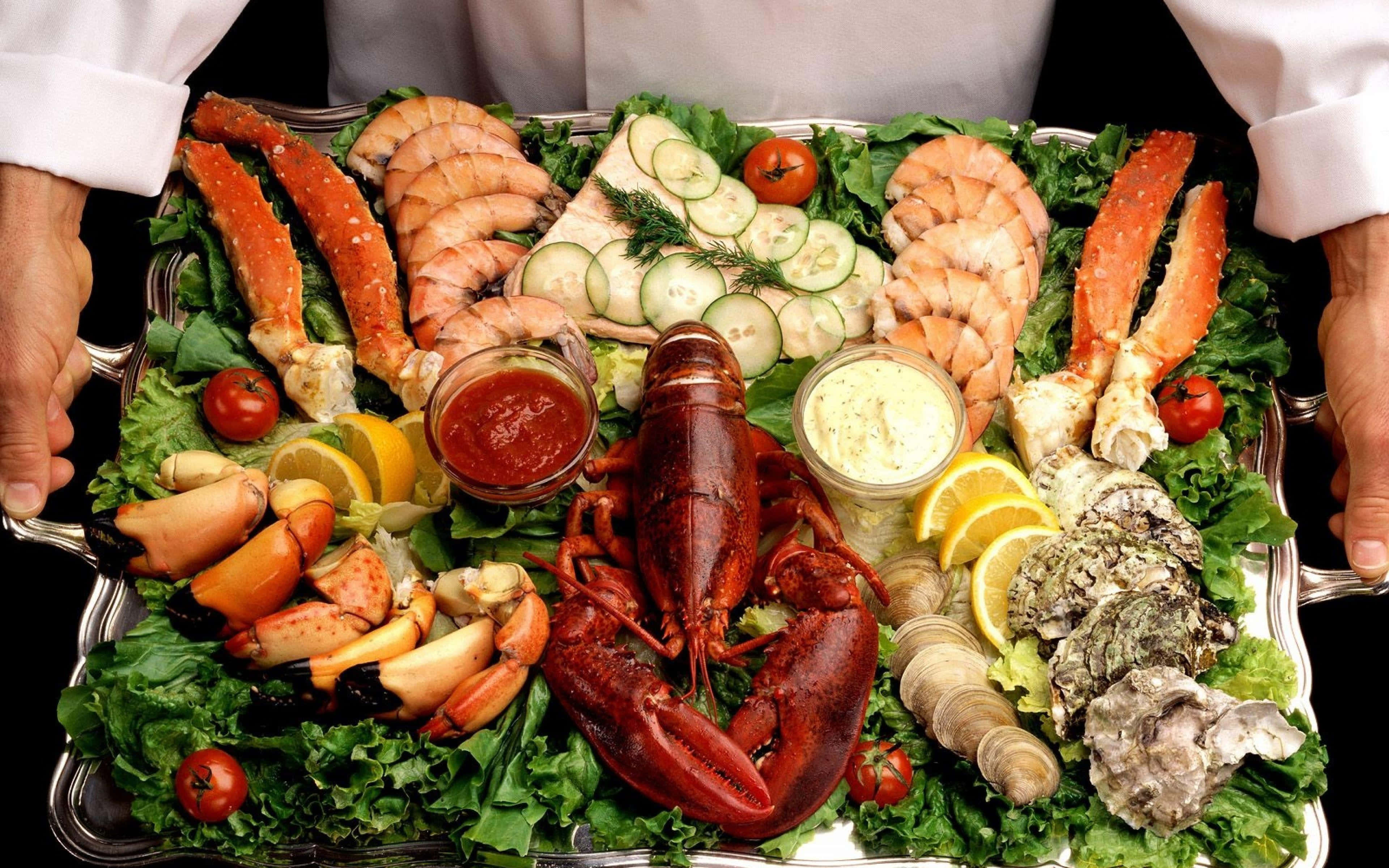 Seafood 桌布 壁紙 — 一位廚師在銀托盤上展示豐盛的海鮮拼盤，包括龍蝦、蟹鉗、蝦、生蠔和裝飾。