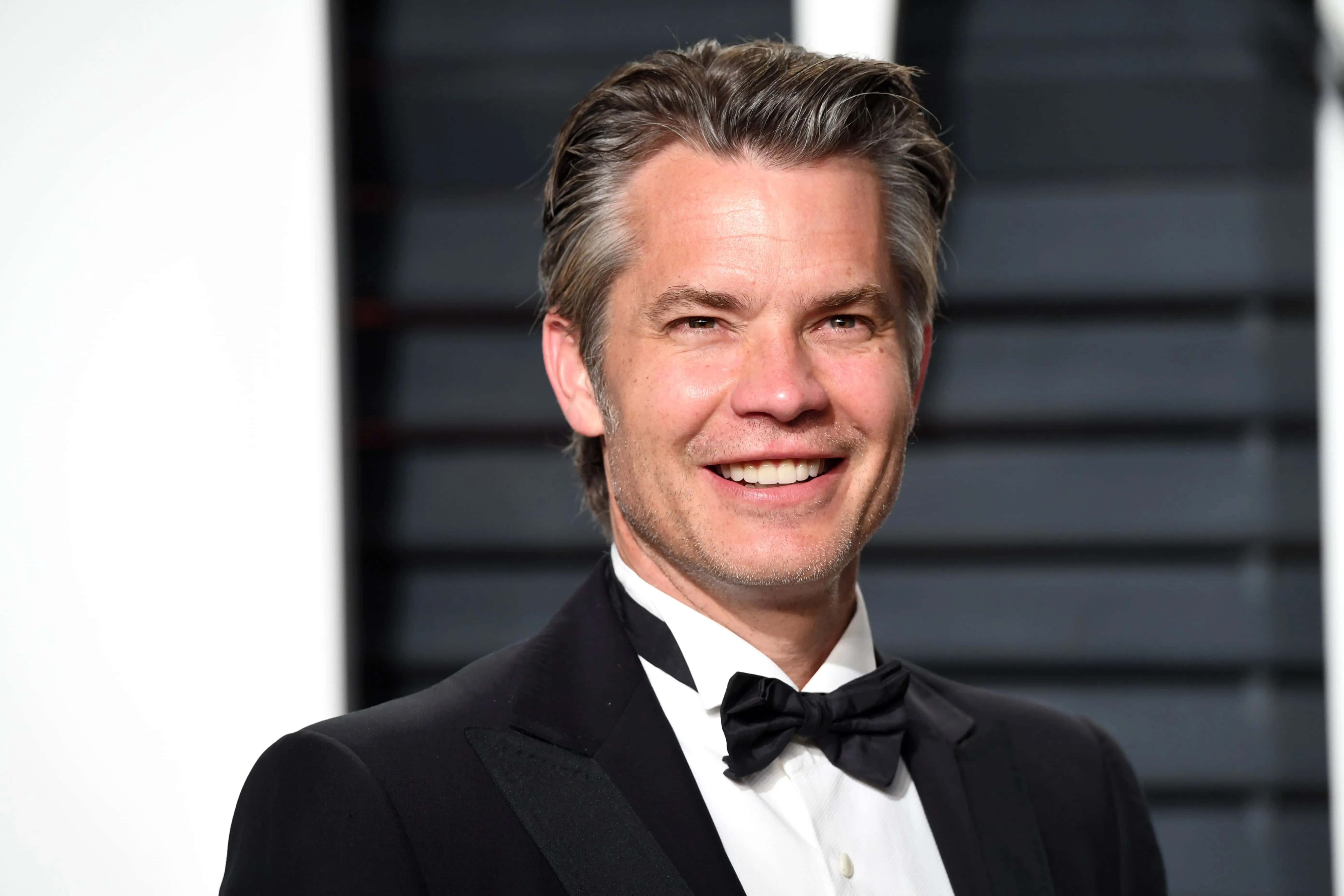 timothy olyphant 桌布 壁紙 — 一位微笑嘅男人，身穿黑色禮服同蝴蝶結，喺深色條紋背景前擺姿勢。