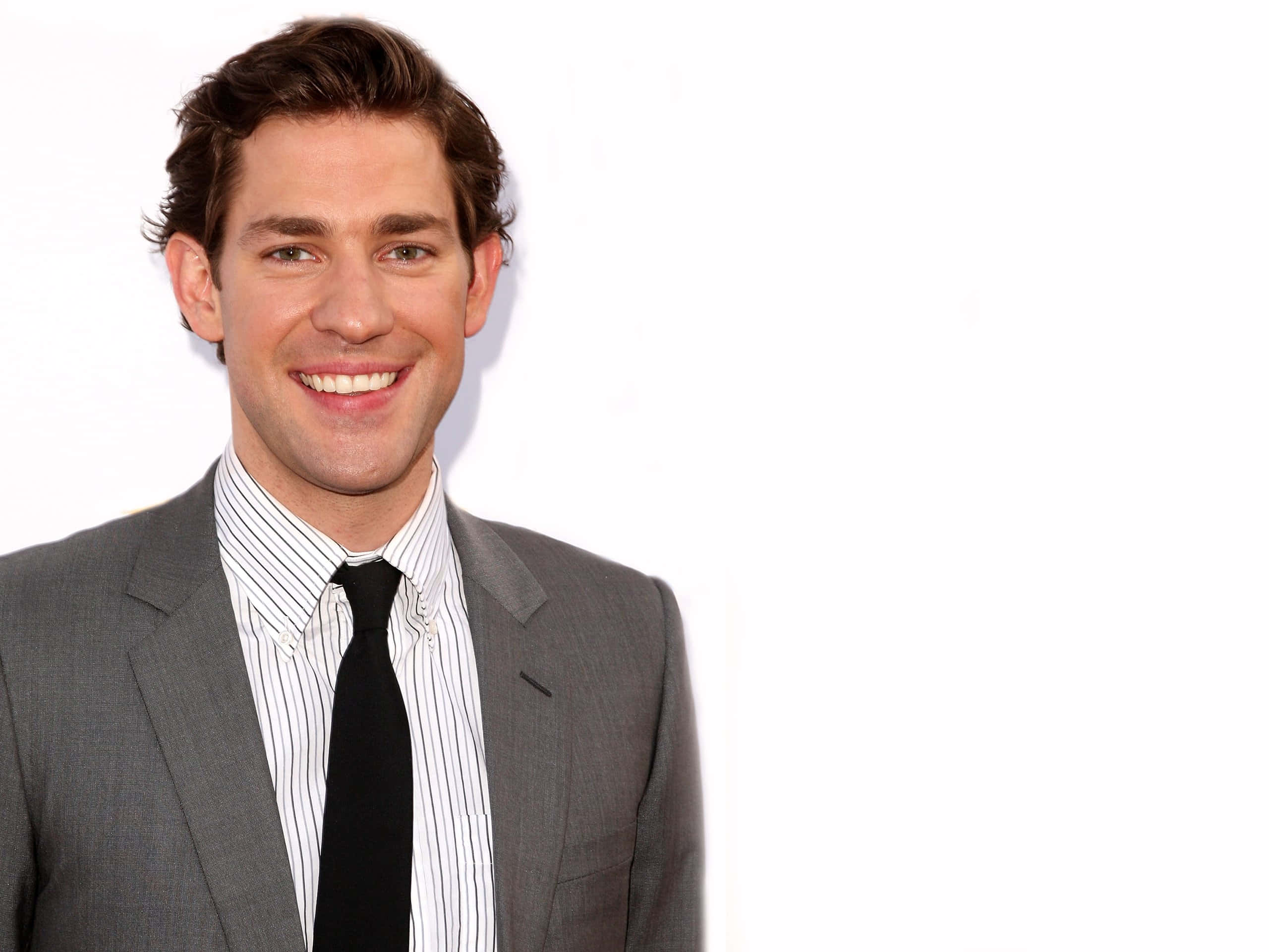 john krasinski 桌布 壁紙 — 一位微笑嘅男士，身穿灰色西裝同條紋恤衫，喺純白色背景前擺甫士。
