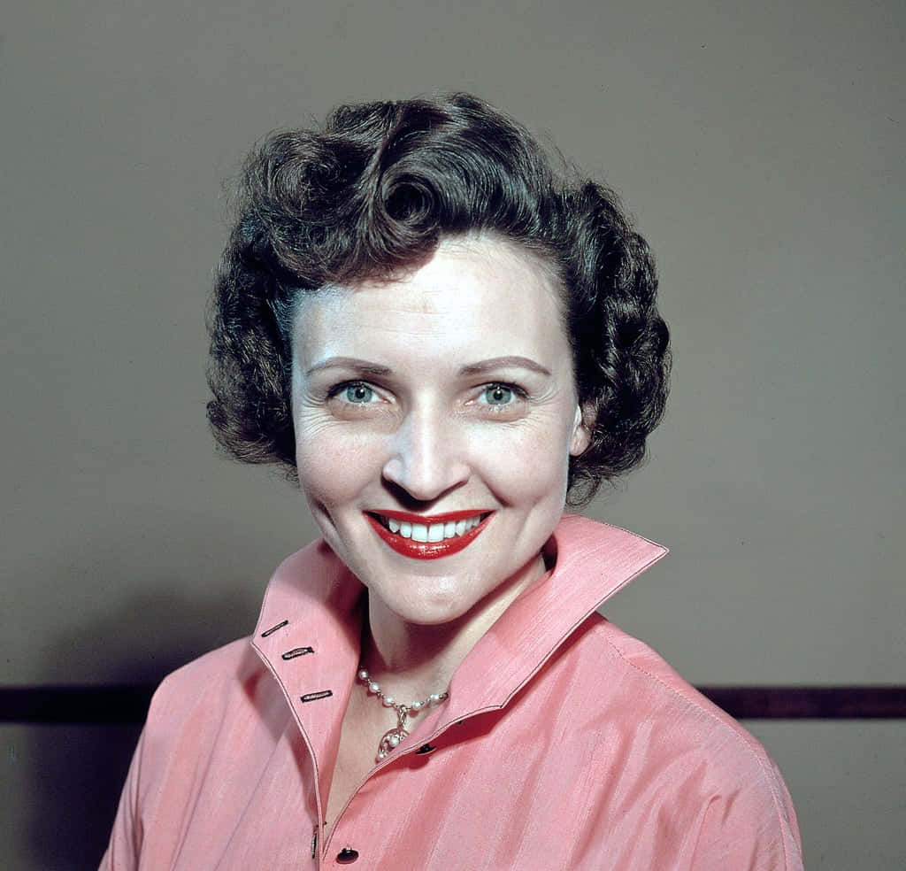 Betty White 桌布 壁紙 — 一位微笑女士的復古肖像，她擁有深色捲髮和紅色唇膏，穿著粉紅色有領襯衫。