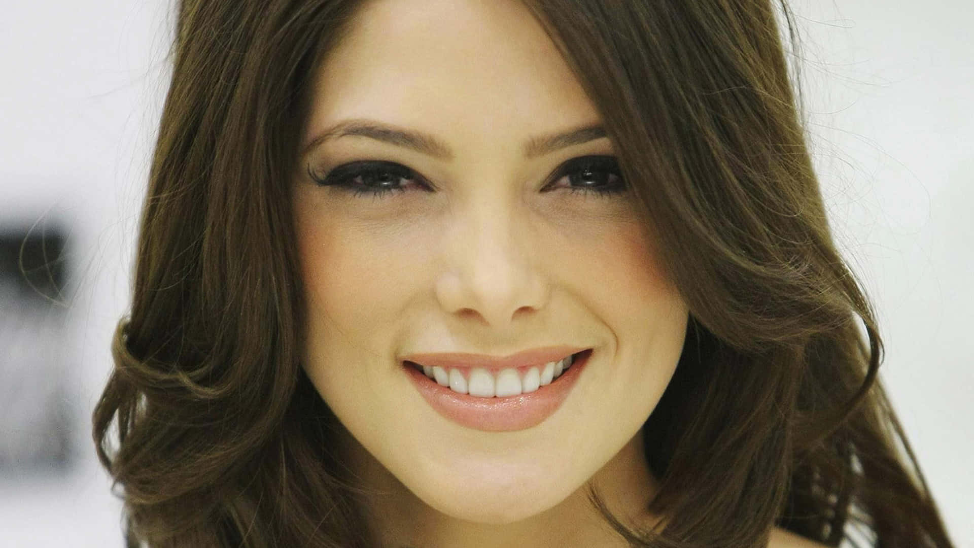 ashley greene 桌布 壁紙 — 一位微笑女性的特寫肖像，擁有深色波浪髮和明亮的眼睛，背景柔和模糊。