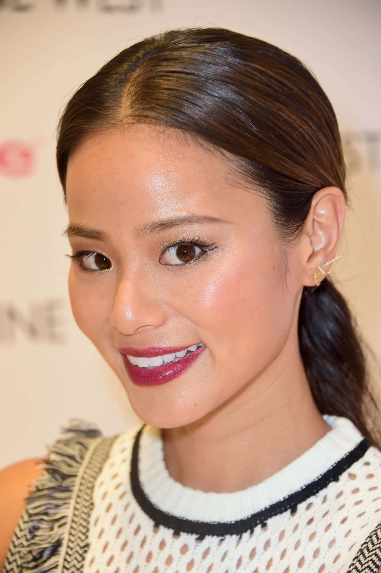 Jamie Chung 桌布 壁紙 — 一位微笑女性的特寫肖像，深色頭髮紮成馬尾，身穿白色針織上衣搭配黑色飾邊和鮮豔的紅色唇膏。