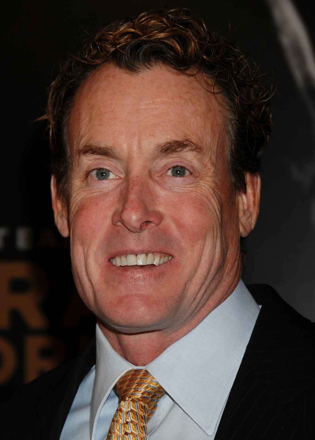 John C. Mcginley 桌布 壁紙 — 一位微笑男士的 close-up 肖像，他擁有棕色捲髮，身穿深色西裝和金色圖案領帶。