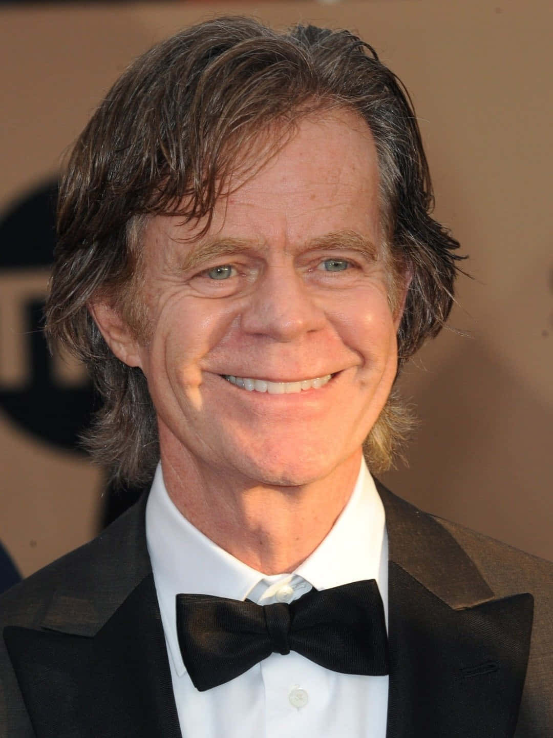 william h. macy 桌布 壁紙 — 一位微笑男士的近距離肖像照，他有一頭波浪棕色頭髮，身穿黑色燕尾服並佩戴蝴蝶結領結。