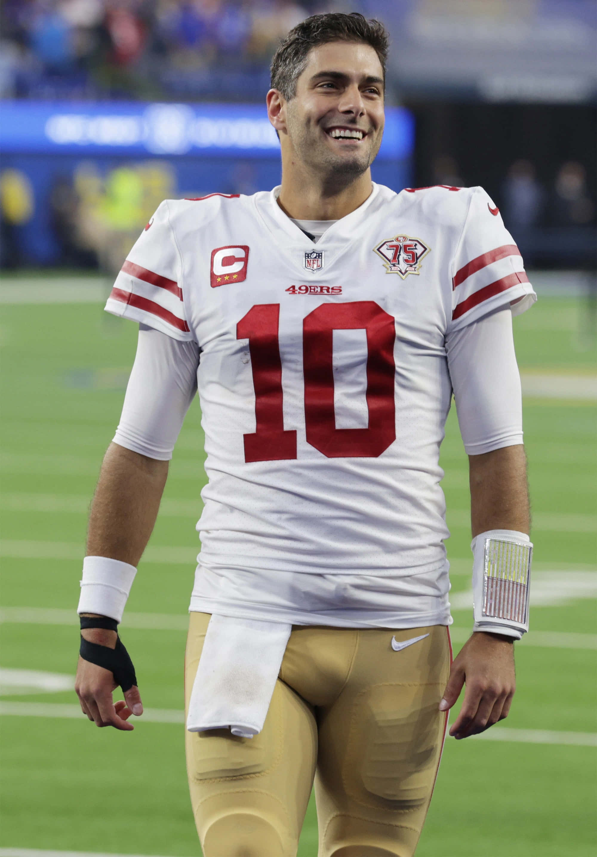 Jimmy Garoppolo 桌布 壁紙 — 一位微笑的三藩市49人四分衛，身穿白色和紅色10號球衣，在綠色足球場上行走。