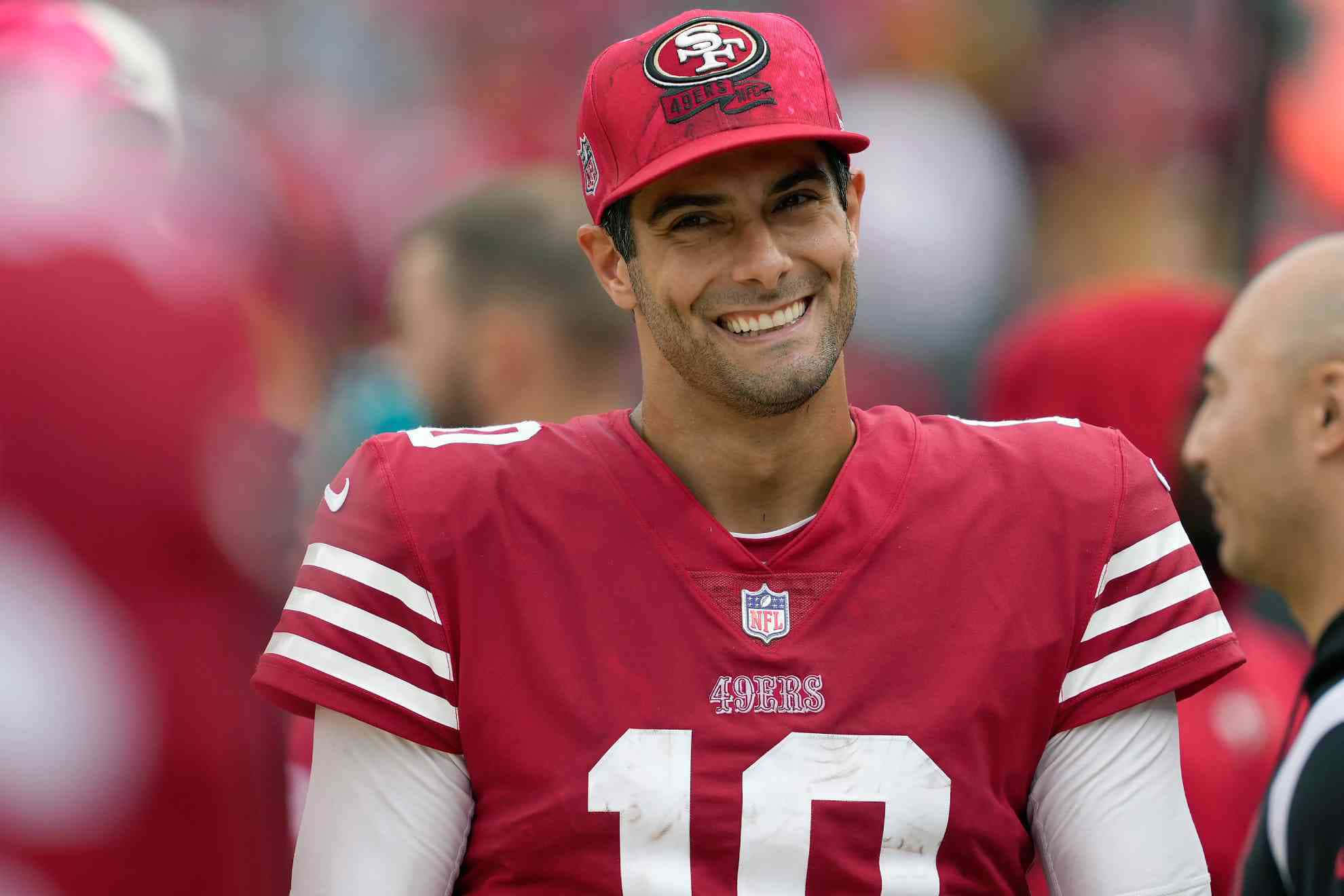 Jimmy Garoppolo 桌布 壁紙 — 一位微笑的三藩市49人隊四分衛，身穿紅色10號球衣，在陽光明媚的比賽日對著鏡頭綻放光芒。