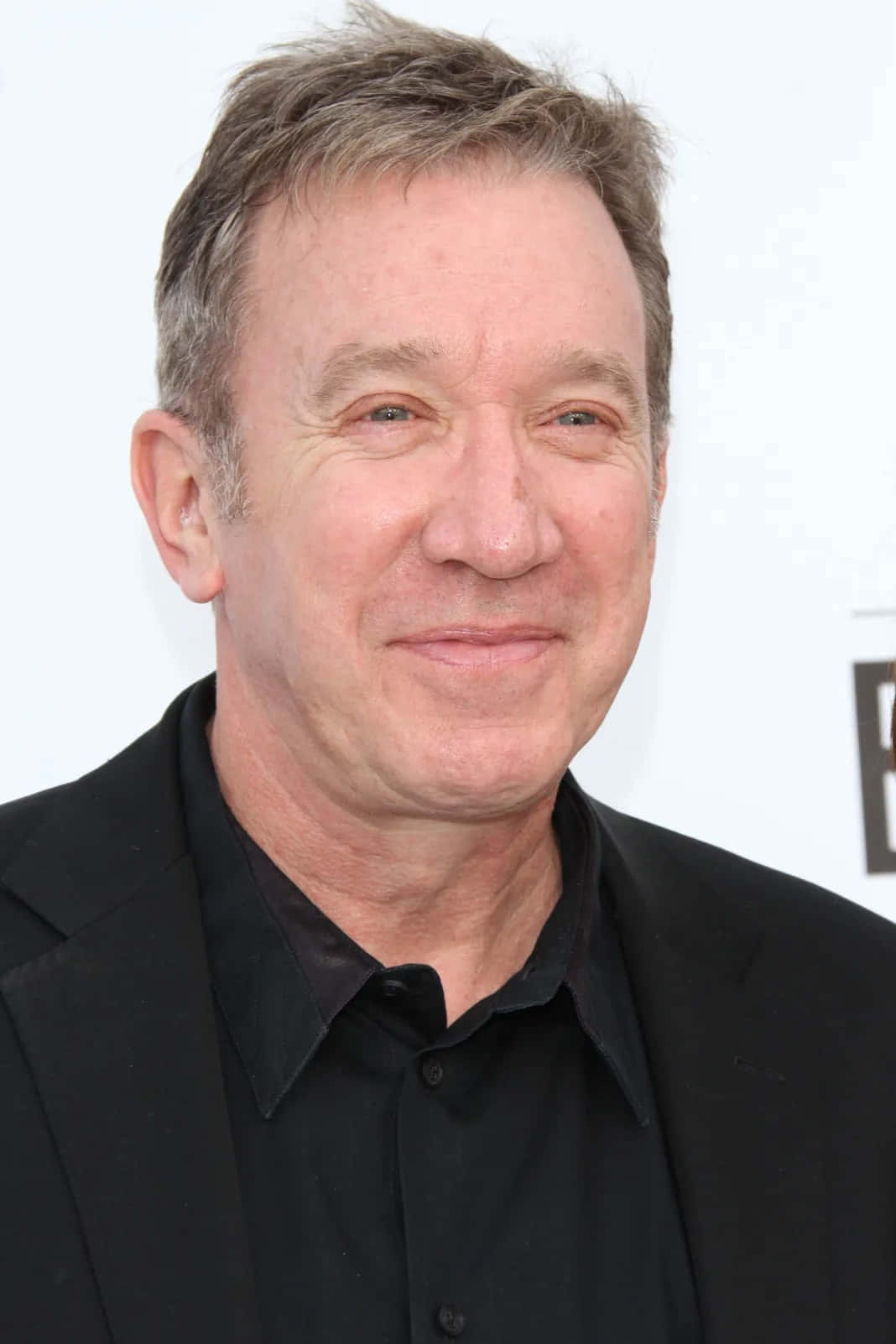 Tim Allen 桌布 壁紙 — 一位微笑的中年男子，灰白頭髮，身穿黑色西裝和襯衫，背景為白色的特寫肖像。