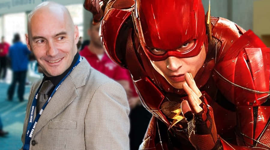 Grant Morrison 桌布 壁紙 — 一位微笑的光頭男士穿著格紋西裝，站在一位身穿閃亮紅色服裝、帶有閃電標誌的超級英雄旁邊。