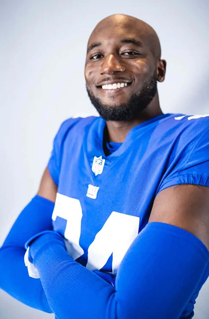 James Bradberry 桌布 壁紙 — 一位微笑的光頭黑人足球員，身穿藍色球衣，雙臂交叉，背景為純白色。