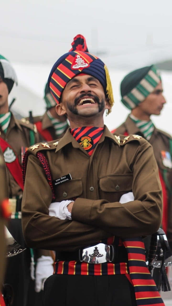 Indian Army 桌布 壁紙 — 一位微笑的印度士兵穿著禮儀制服，戴著彩色頭巾和條紋圍巾，自信地交叉雙臂站立。