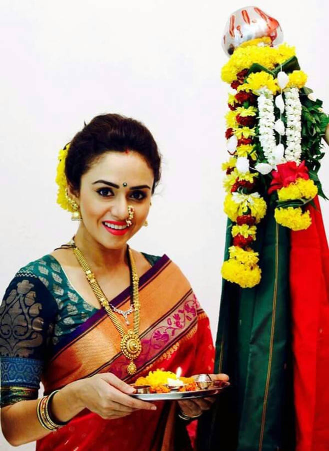 Gudi Padwa 桌布 壁紙 — 一位微笑的女士穿著傳統印度服飾，在裝飾著鮮豔黃色和白色花朵的燈柱旁，手持一盞點燃的迪亞燈。