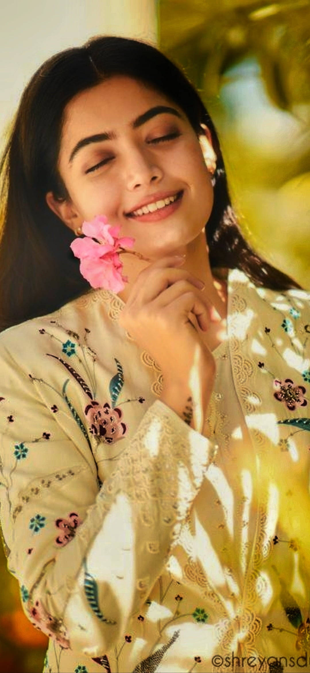telugu 桌布 壁紙 — 一位微笑的女子閉著眼睛，在溫暖的金色陽光下輕輕將一朵粉紅花靠近臉頰。