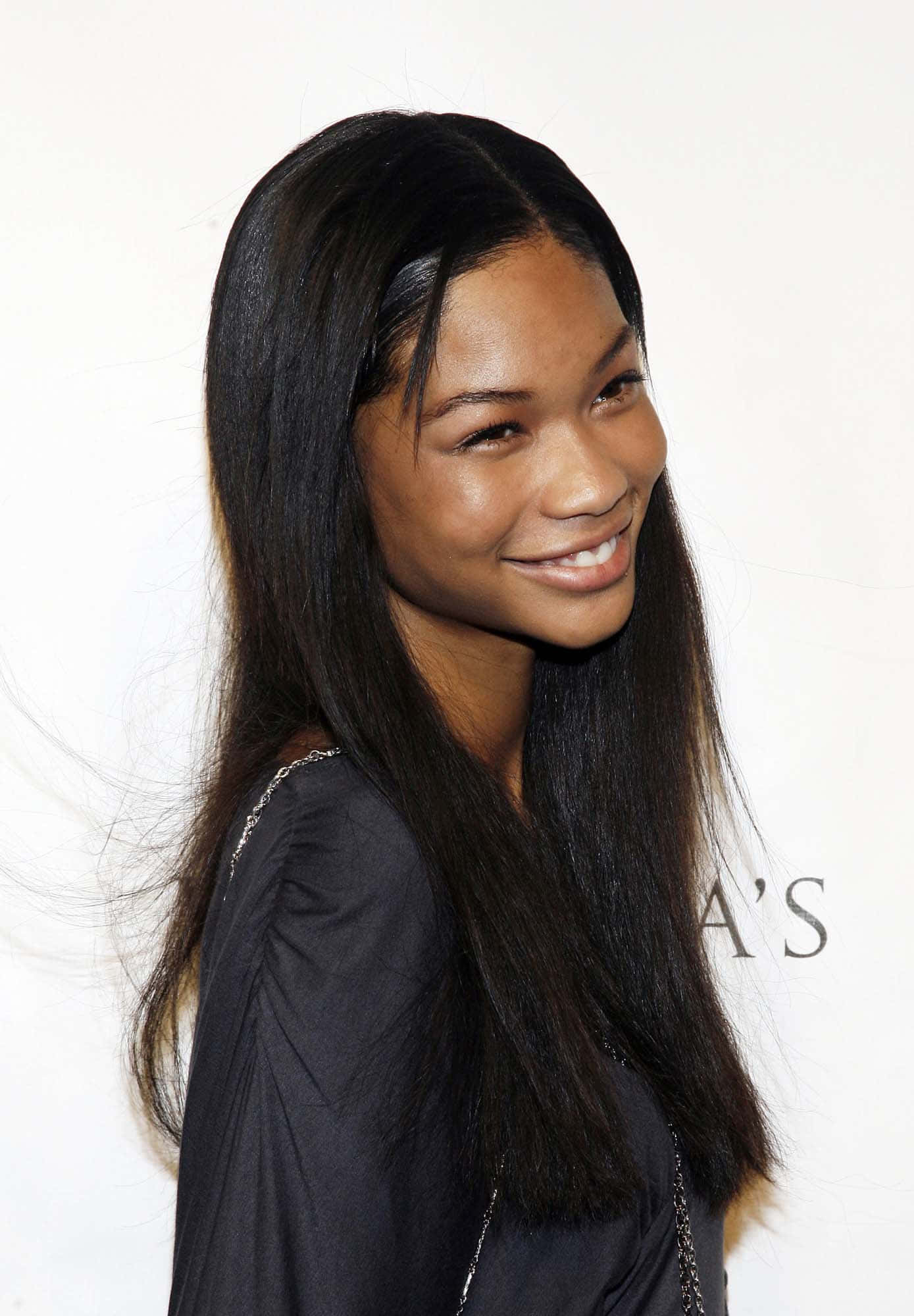 chanel iman 桌布 壁紙 — 一位微笑的女性，擁有長直黑髮和黑色上衣，背景為純白色。