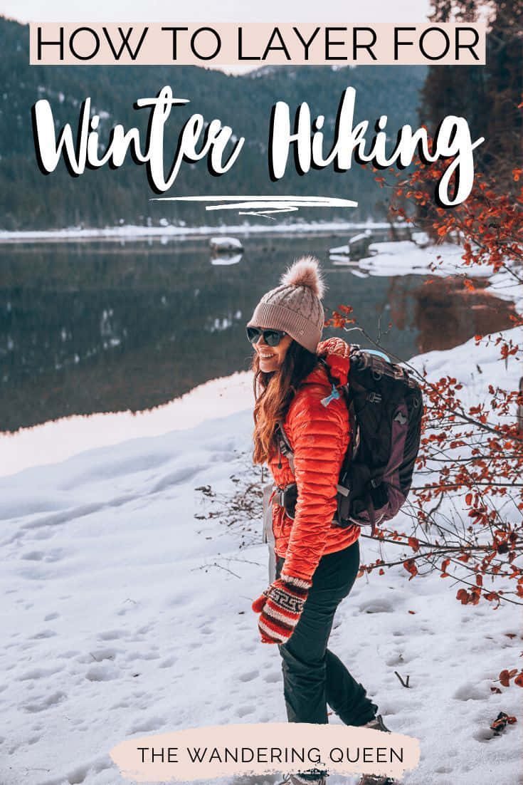 Winter Hiking 桌布 壁紙 — 一位微笑的女性穿著亮橙色外套和粉紅色冷帽，在雪地中徒步，旁邊是平靜、覆蓋薄雪的湖泊，背景是樹木繁茂的山丘。