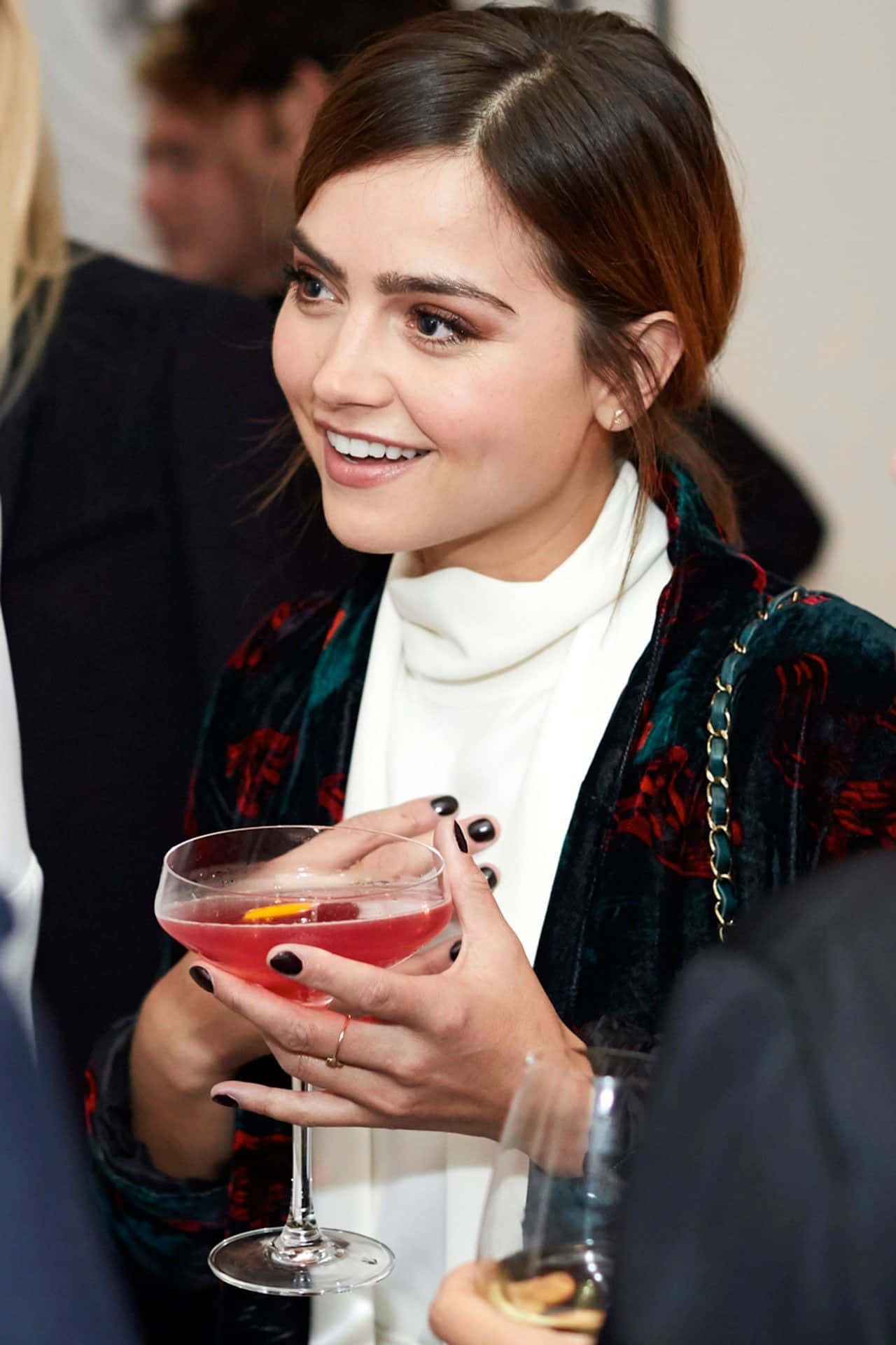 Jenna Coleman 桌布 壁紙 — 一位微笑的女性穿著天鵝絨外套，在社交聚會中手持粉紅色雞尾酒。