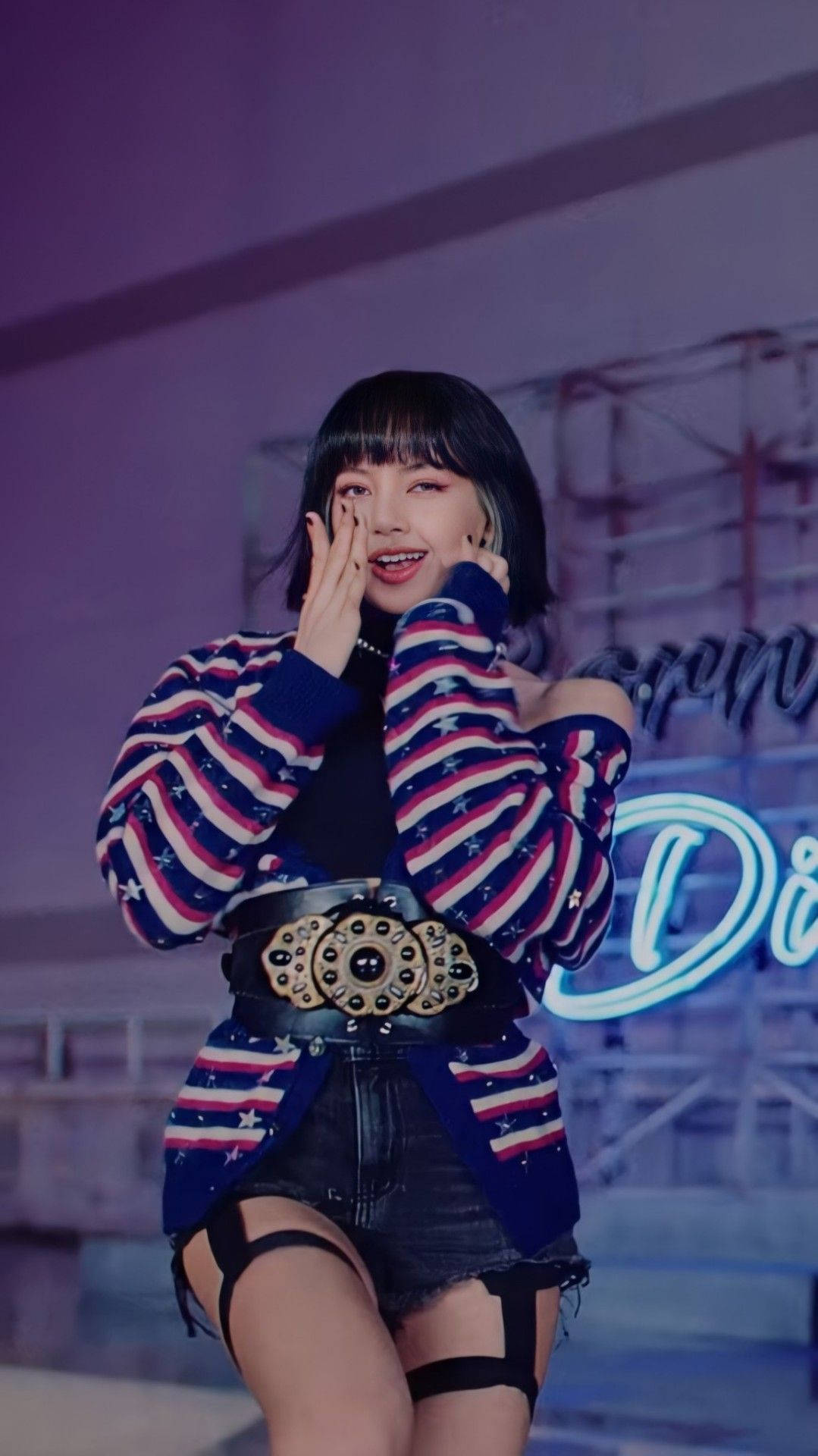 Lalisa Manoban Love Sick Girls 壁紙 — 一位微笑的女性穿著星星圖案毛衣和牛仔短褲，在紫色舞台燈光下將手靠近臉部擺姿勢。
