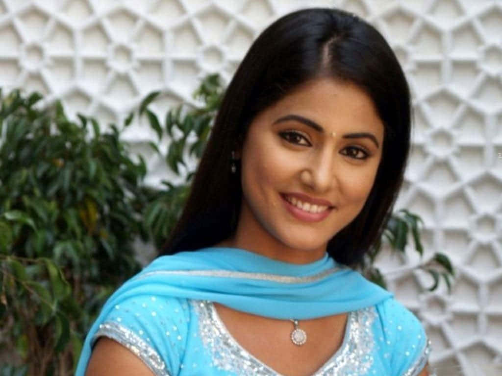 Indian Girl 桌布 壁紙 — 一位微笑的女性身穿亮藍色傳統服裝，站在帶有綠色葉子的白色幾何牆前。