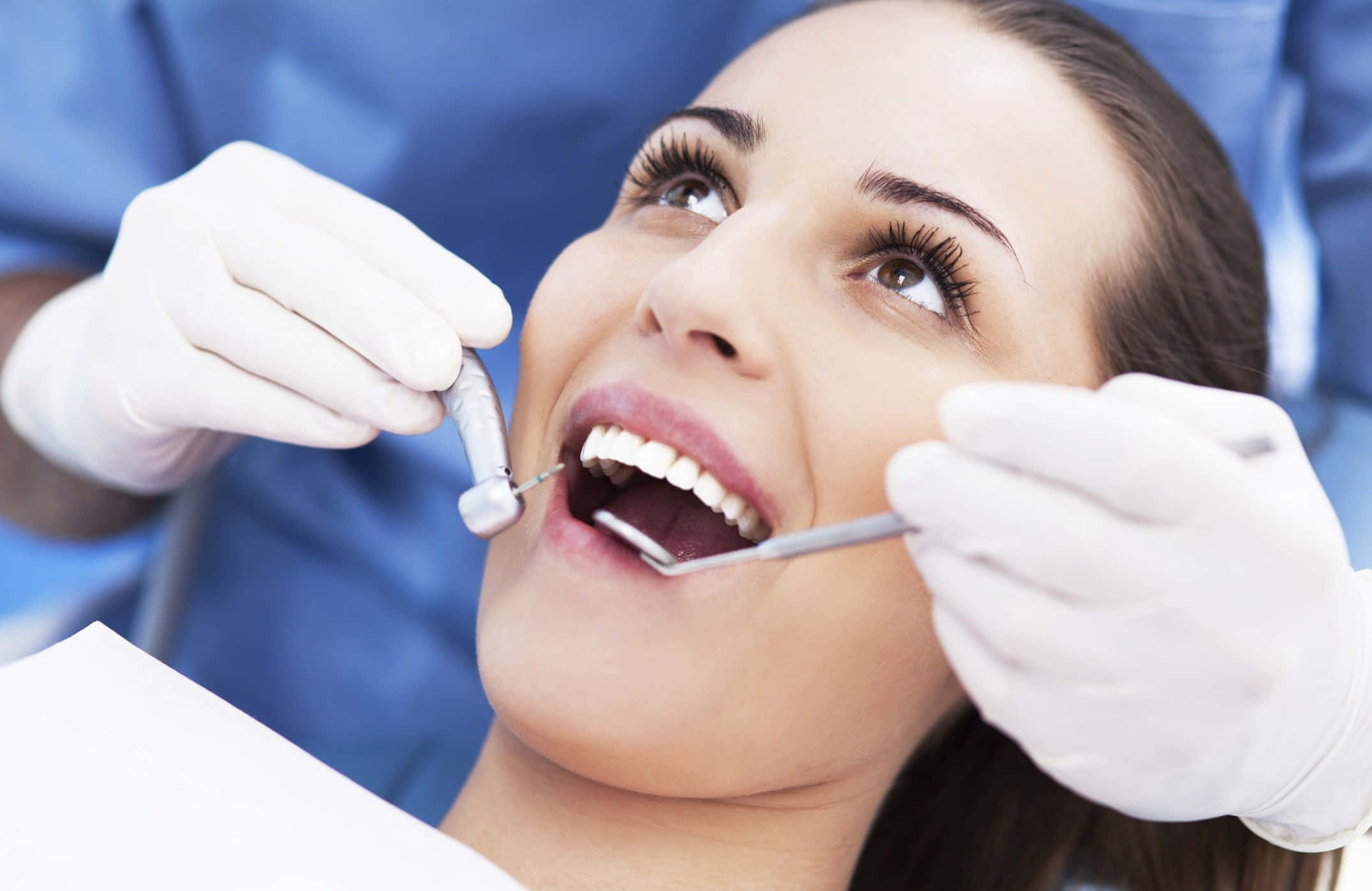 Dentist 桌布 壁紙 — 一位微笑的女性躺在牙科椅上，戴著手套的手用工具檢查她亮白的牙齒。