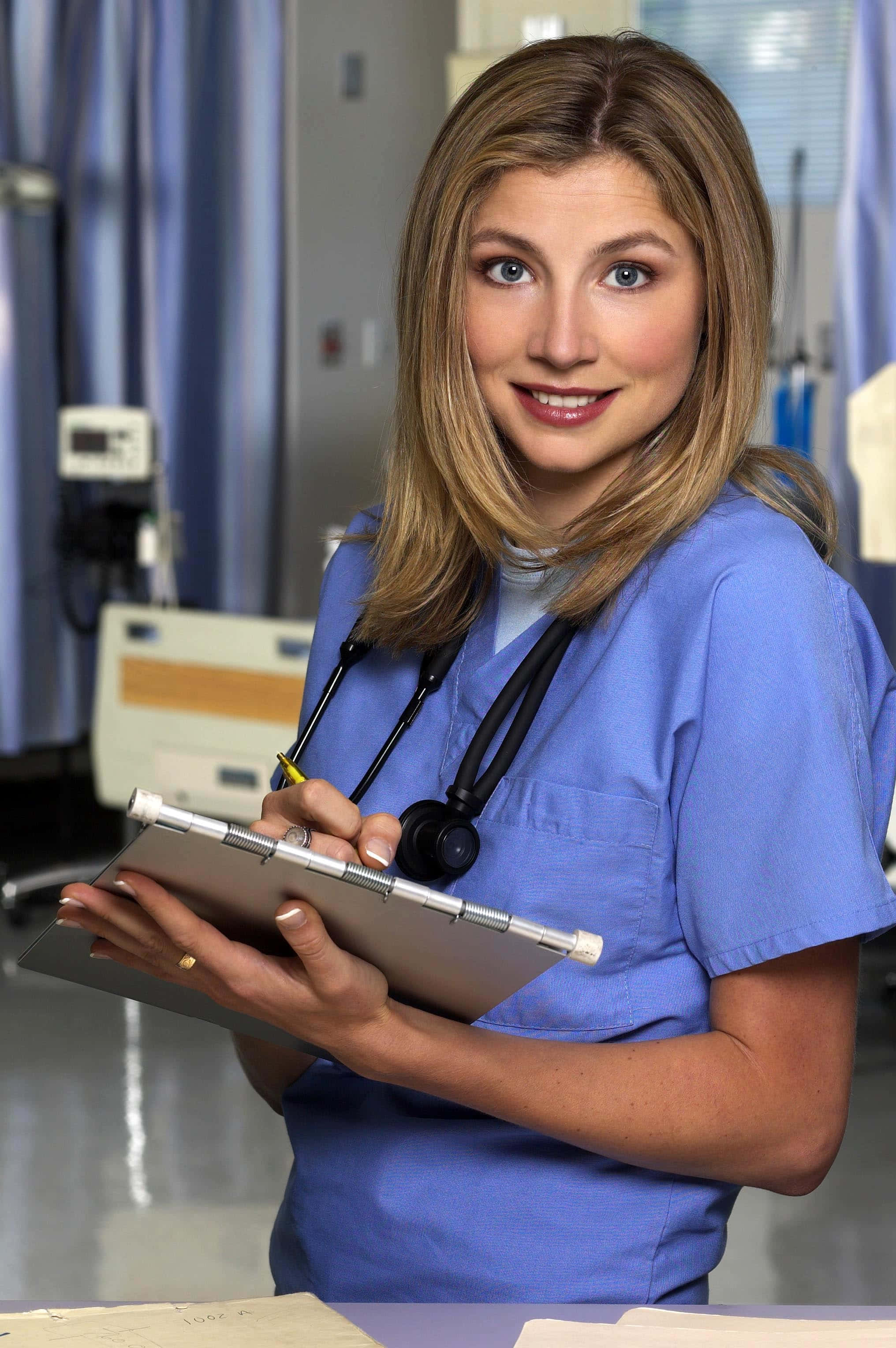 Sarah Chalke 桌布 壁紙 — 一位微笑的女護士穿著藍色工作服，頸上掛著聽診器，在醫院房間裡拿著夾板。