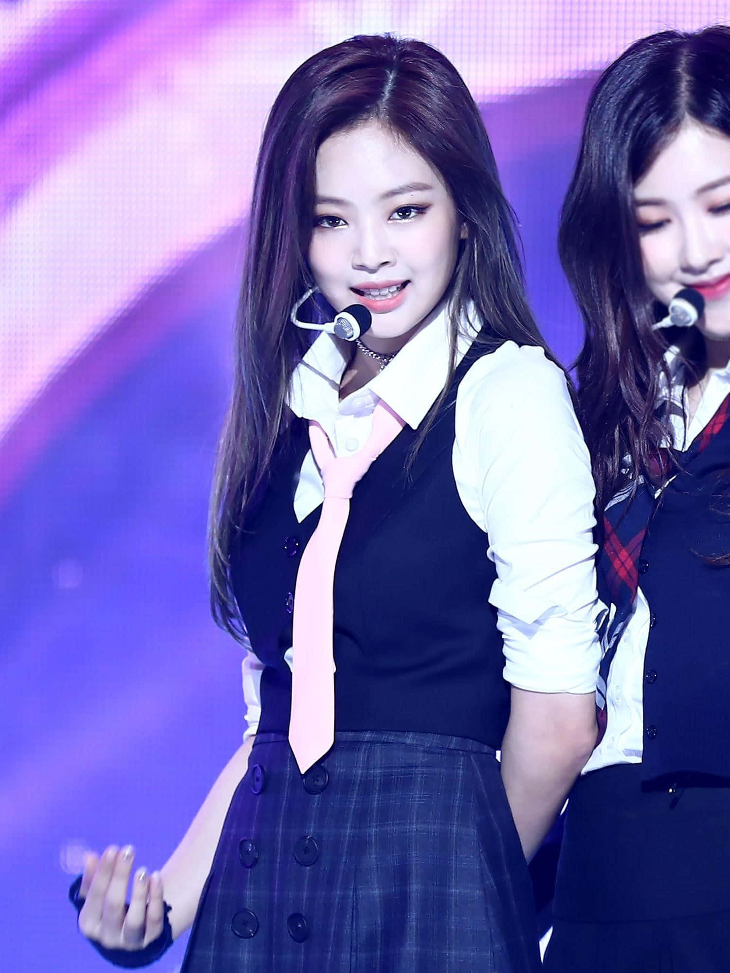 Jennie Kim 桌布 壁紙 — 一位微笑的年輕女子穿著校服，繫著粉紅色領帶，在充滿活力的紫色燈光舞台上表演。