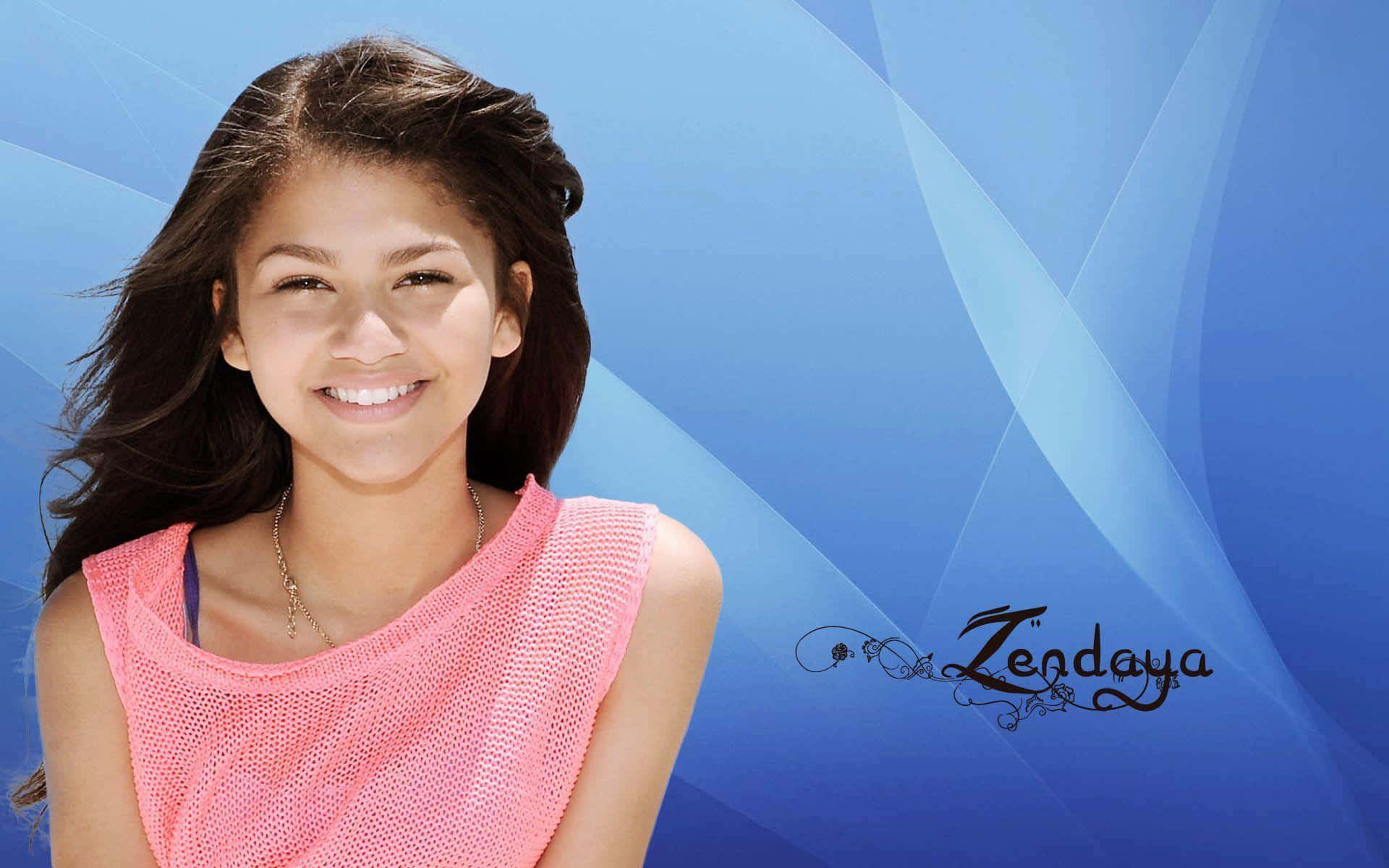 Zendaya 桌布 壁紙 — 一位微笑的年輕女性，深色頭髮，穿著粉紅色上衣，站在藍色抽象背景前，附近有她的名字書寫。