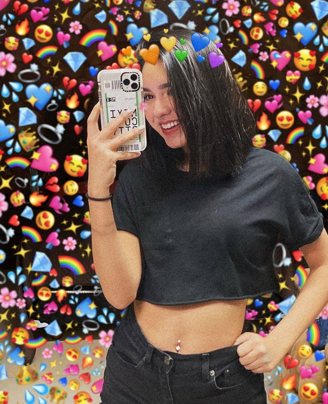 Tik Tok 桌布 壁紙 — 一位微笑的年輕女性在充滿活力的表情符號牆紙前自拍，牆紙上有心形、彩虹和鑽石。