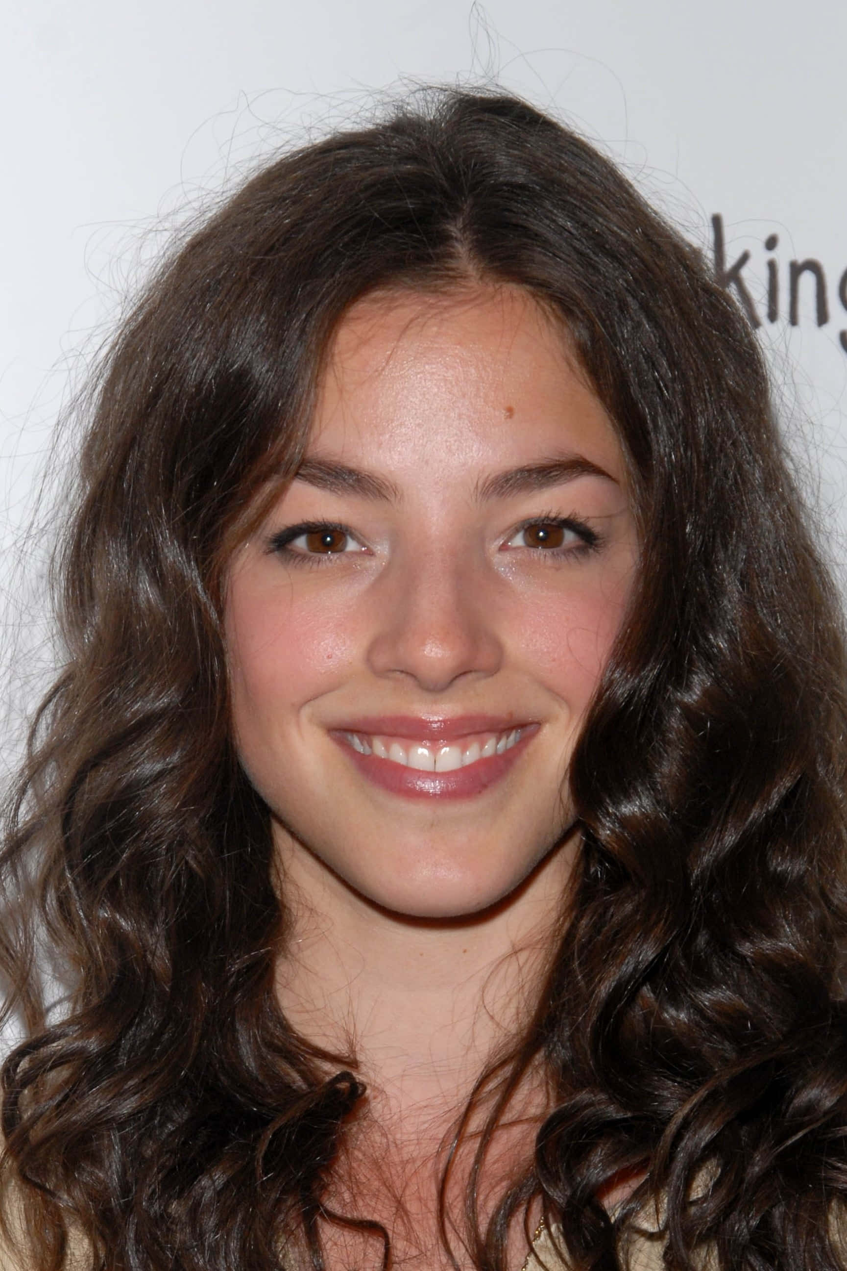 Olivia Thirlby 桌布 壁紙 — 一位微笑的年輕女性近距離肖像，擁有長長的波浪形棕色頭髮和溫暖的棕色眼睛。