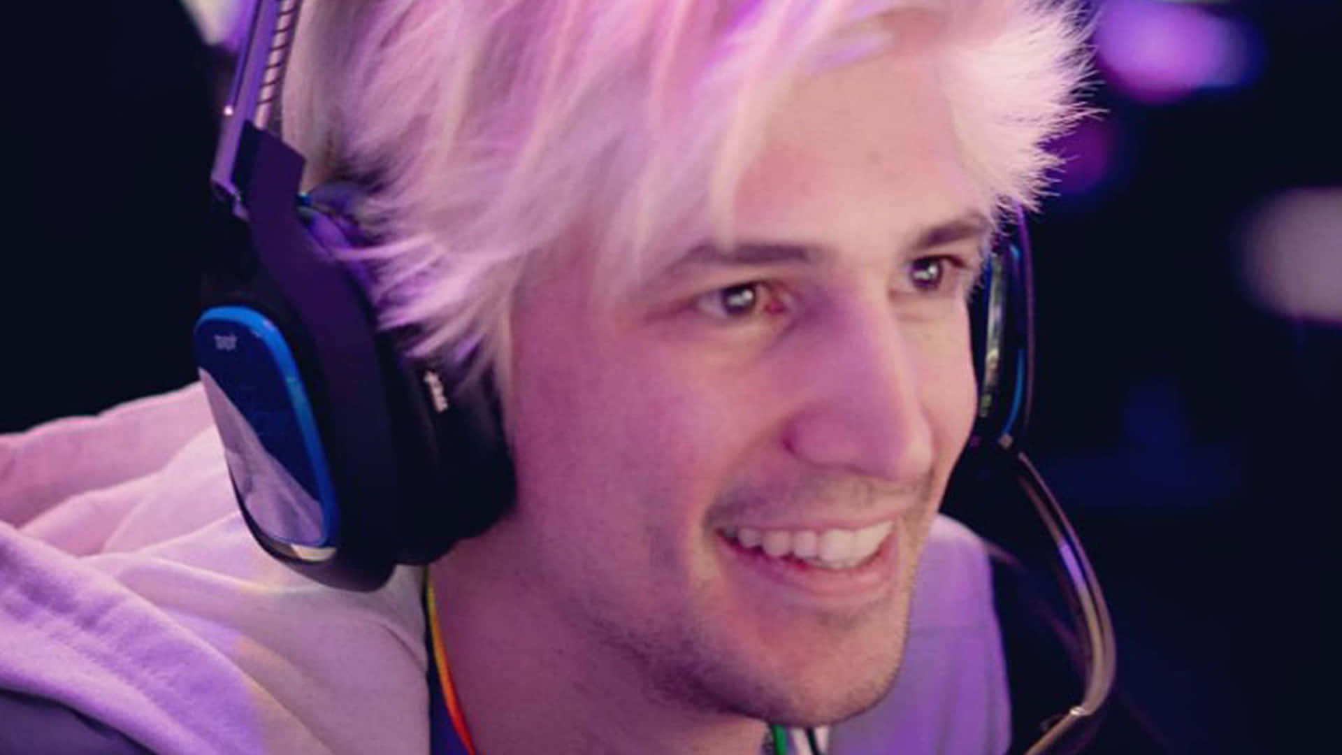 Minecraft Twitch Streamers 桌布 壁紙 — 一位微笑的年輕男子，留著鉑金色頭髮，在紫色環境燈光下戴著遊戲耳機。