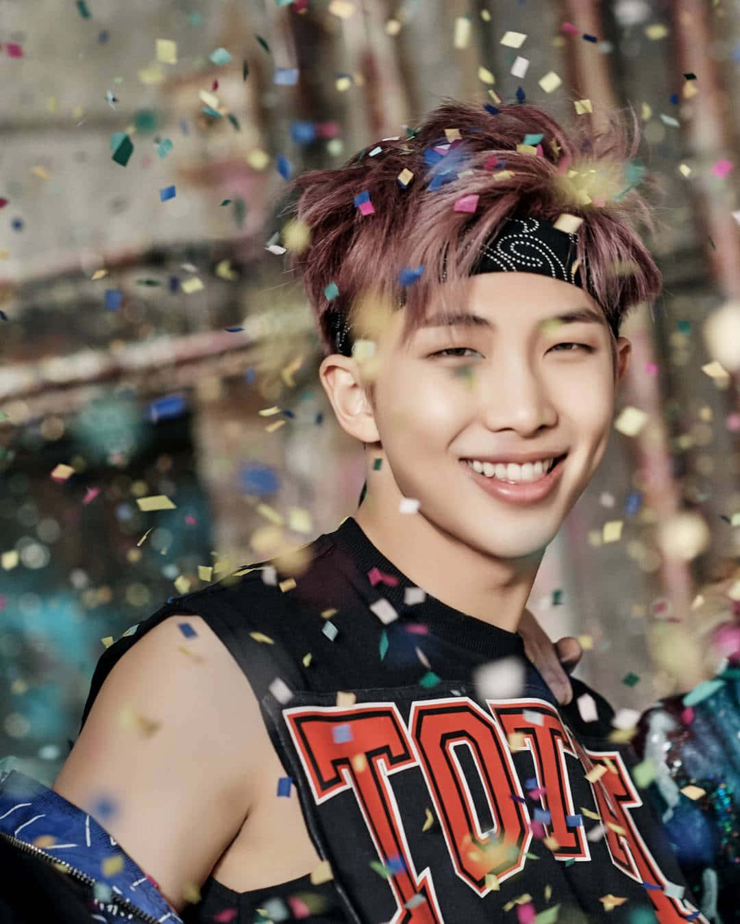 Bts Rap Monster 桌布 壁紙 — 一位微笑的年輕男子，粉紅色頭髮和頭帶，在五彩紙屑如雨般落在他周圍時閃耀著光芒。