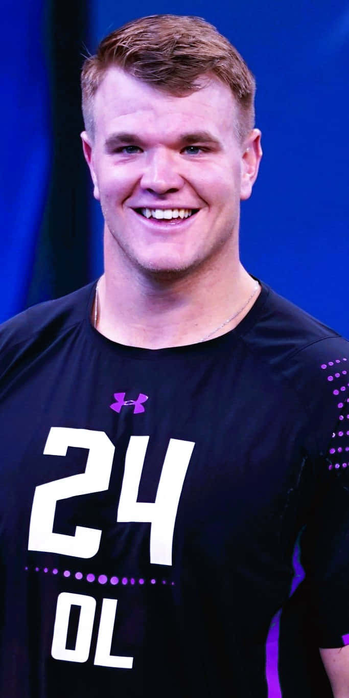 Mike Mcglinchey 桌布 壁紙 — 一位微笑的年輕足球員，身穿黑色Under Armour球衣，上面有24號和OL字樣，站在藍色背景前。
