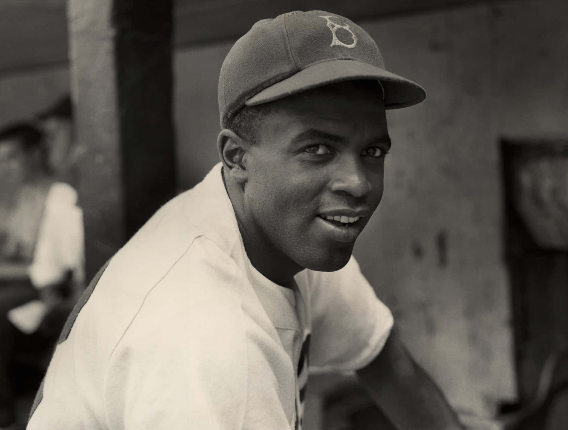 Jackie Robinson 桌布 壁紙 — 一位微笑的棒球運動員，戴著復古帽子和穿著復古制服，在經典的黑白肖像中直視鏡頭。