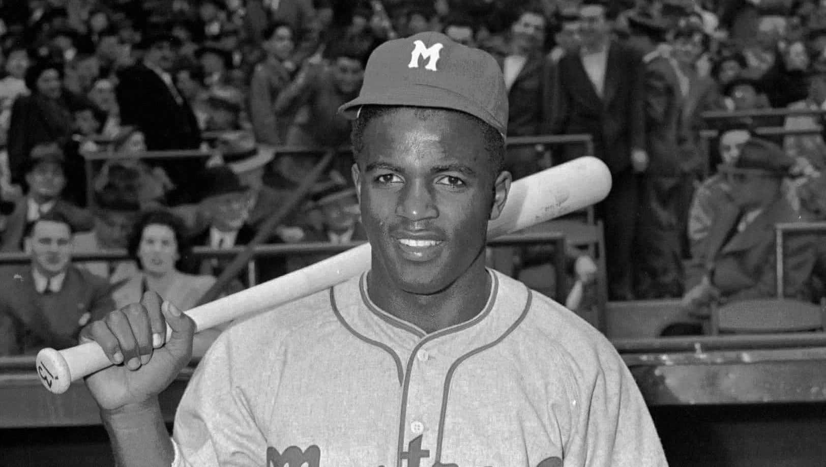 Jackie Robinson 桌布 壁紙 — 一位微笑的棒球運動員穿著復古球衣，在擠滿觀眾的球場上將球棒扛在肩上。