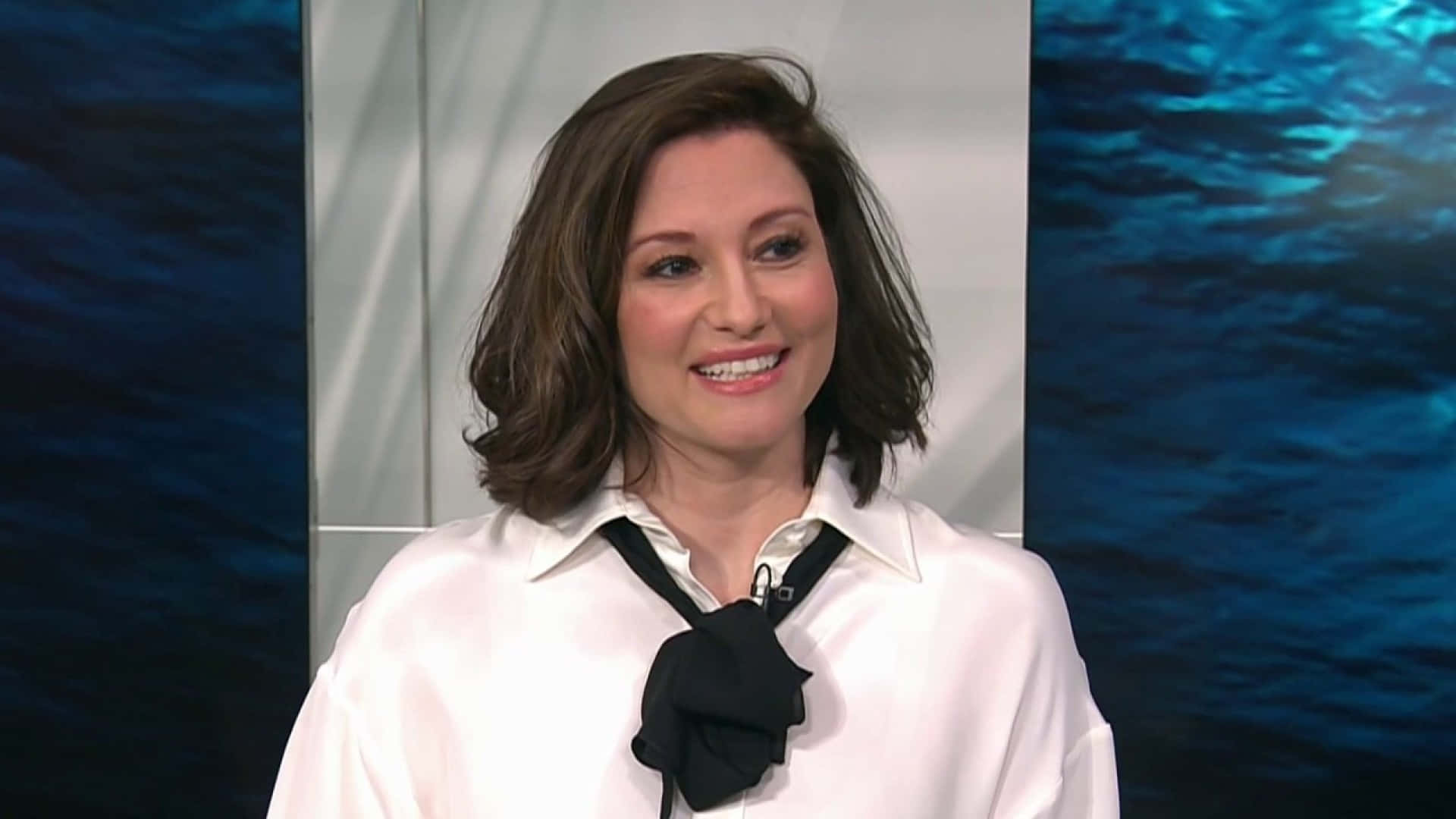 Chyler Leigh 桌布 壁紙 — 一位微笑的棕髮女性，穿著白色襯衫配黑色蝴蝶結，背景是藍色水主題。